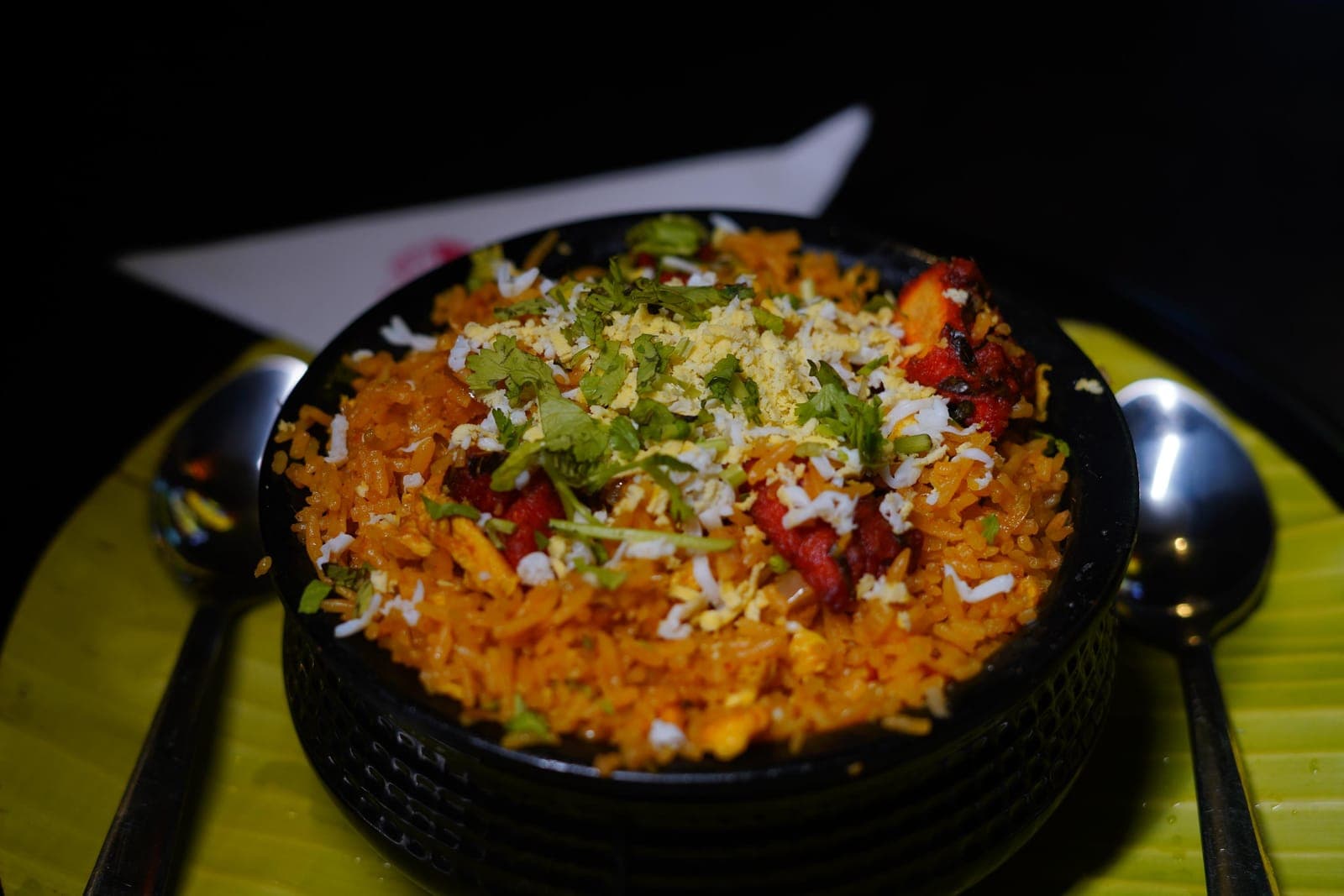 Egg kothu biriyani served in a black bowl with coriander on a banana leaf